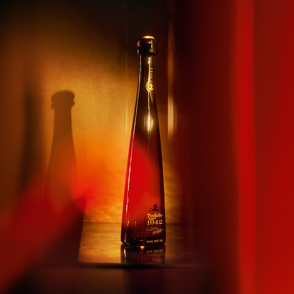 Tequila bottle labeled Don Julio 1942 standing on a wooden bar with warm amber lighting.