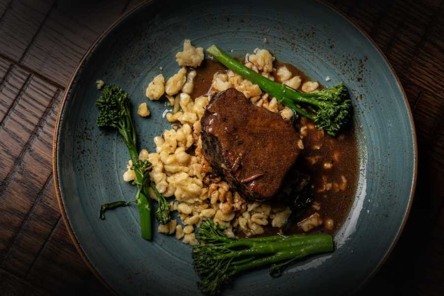 square-22-strongsville-ohio 1 | Square 22 Restaurant and Bar Braised beef short rib with barley and broccolini on a blue plate, green vegetables surrounding the meat in a brown sauce.